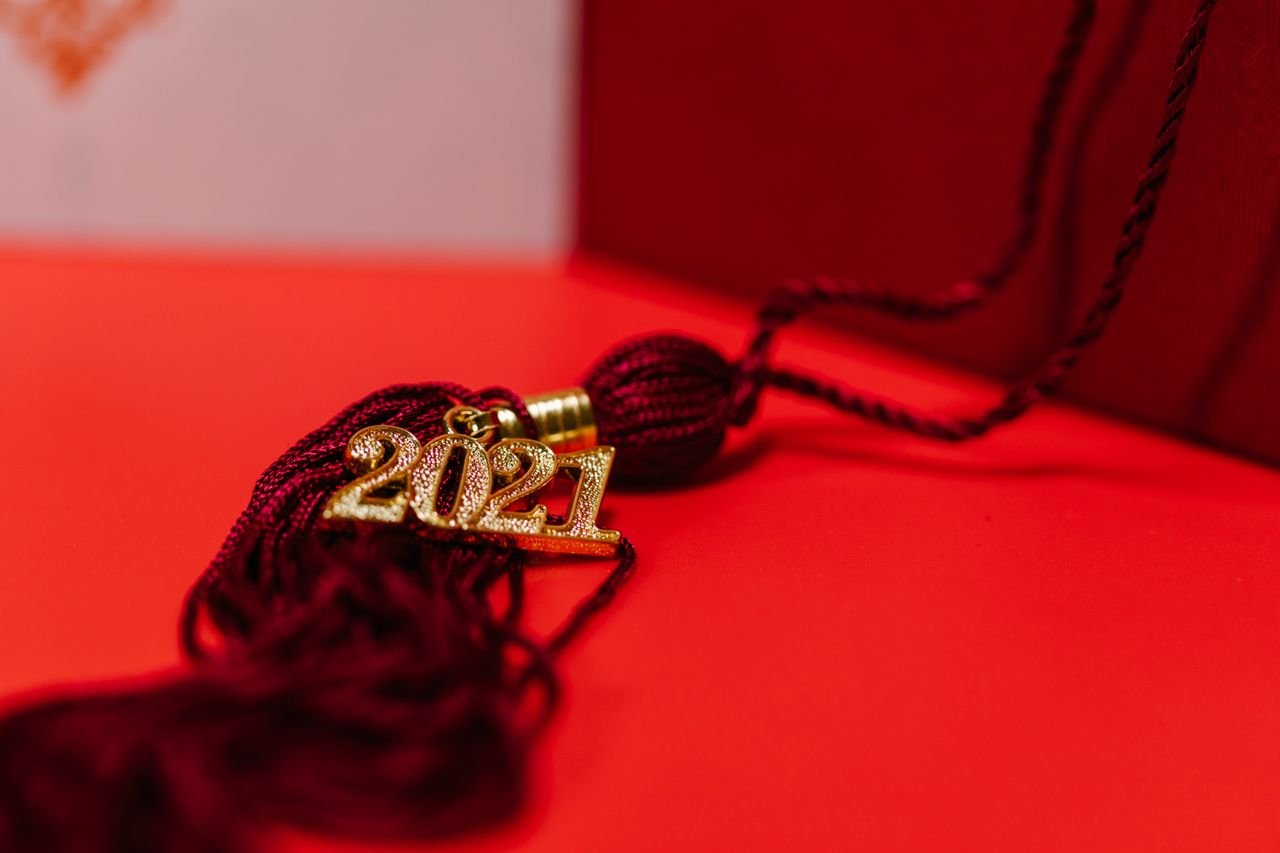 Close-up of a red graduation tassel featuring a gold 2021 charm on a vibrant red background.